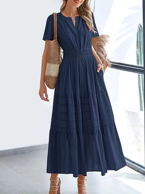 Dark blue ruched V-neck tiered midi dress with short sleeves and pockets, styled with a straw bag.