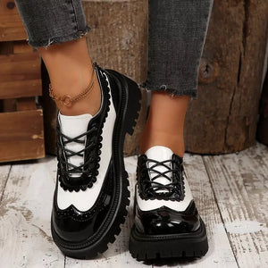 Round toe platform loafers in black and white patent leather with brogue detailing and scalloped trim.