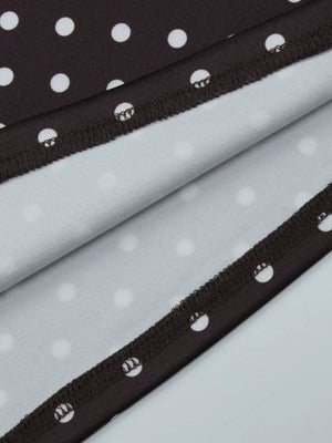 Brown polka dot mini dress detail showing hem with white polka dots on brown fabric.