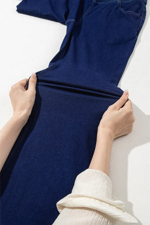 Medium wash denim flare trousers with crossover waist detail shown being stretched.