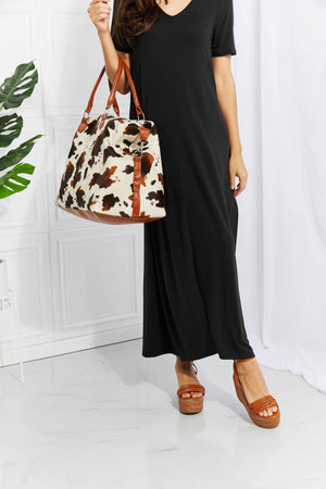 Cowhide print duffel bag with brown leather trim and straps.