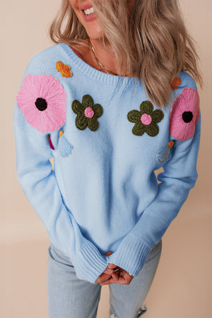 Light blue knit sweater with embroidered floral appliqués and tassels.