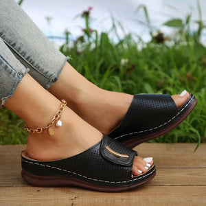 Black perforated wedge sandals with gold accent and white stitching.