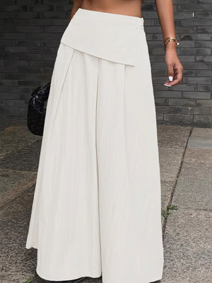 Pleated high-waisted maxi skirt in ivory with button detail and asymmetrical overlay.