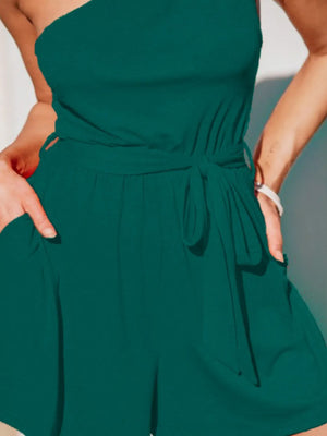 Dark green asymmetrical knot-waist romper with one-shoulder neckline and side pockets.