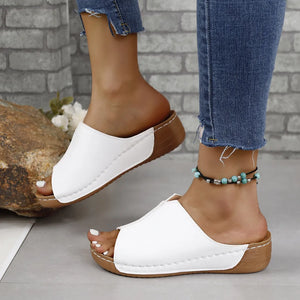 White asymmetrical vegan leather slides with a brown sole and stitching detail.