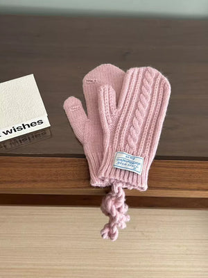 Pink acrylic cable knit mittens with braided detail and attached pom-pom.