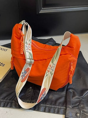 Orange crossbody bag with woven strap featuring floral and surfer motifs.