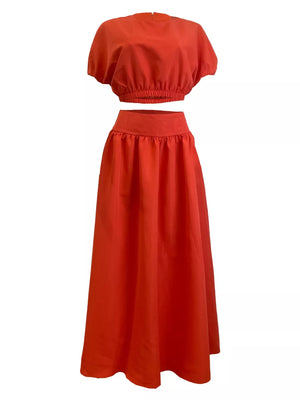 Orange crop top with puff sleeves and elastic hem paired with a high-waisted maxi skirt.