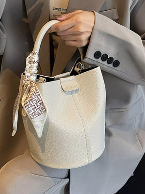 Beige pebbled leather bucket bag with decorative scarf detail on handle