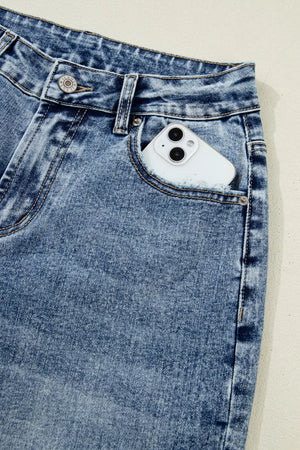 Cuffed mid-rise relaxed fit jeans in distressed blue denim with a phone in the pocket.