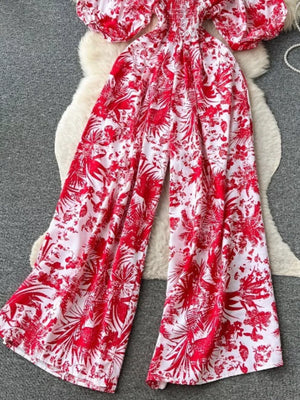 Tropical print smocked wide-leg romper in Scarlet, featuring puff sleeves and a flowy silhouette.