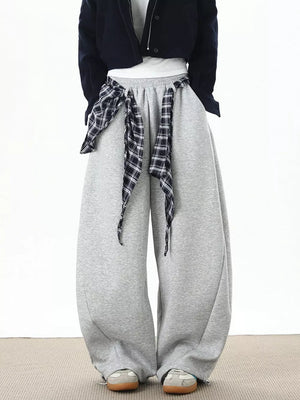 Relaxed fit grey sweatpants with wide legs and drawstring waist, styled with a plaid shirt tied at the waist.