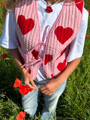 Quilted blush pink tie vest with red heart appliqués and front pockets, styled with a white tee.