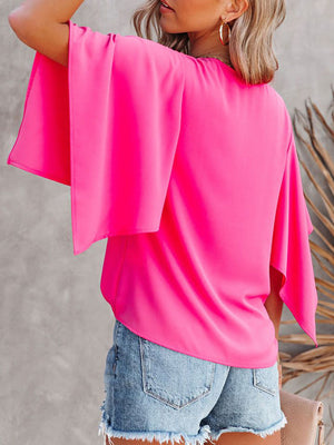 Pink V-neck blouse with wide flutter sleeves, styled with denim shorts.