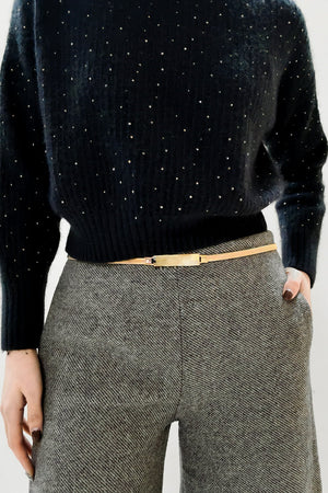 Slimline gold-tone waist belt with a rectangular buckle, worn with a black sequined sweater and grey trousers.