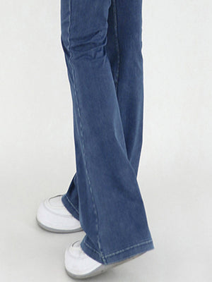 Medium wash denim flare jeans with a crossover waist detail, styled with white sneakers.