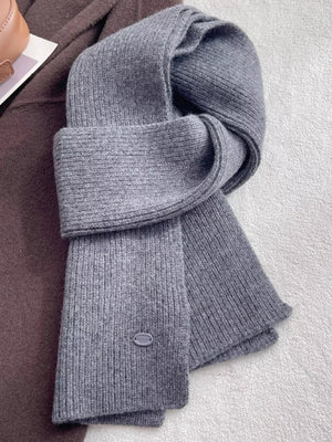 Gray ribbed knit wool scarf with a subtle logo detail, styled with a brown coat.