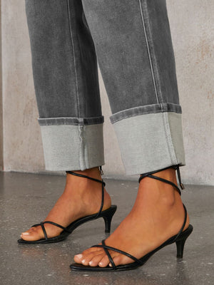 Dark wash denim jeans with wide legs and large cuffs, styled with black strappy kitten heels.