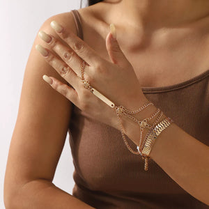 Gold multi-layered chain bracelet with flower accents and a bar detail, worn on hand.