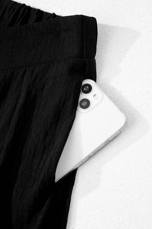 Black textured maternity pants with wide legs and a crossed waist detail, showing a phone in the pocket.
