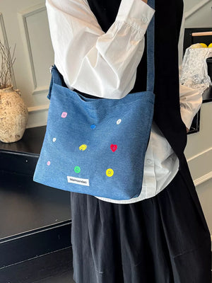 Light blue denim crossbody bag with colorful button embroidery and adjustable strap.