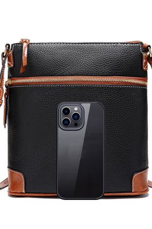 Black leather crossbody bag with brown trim and white stitching, featuring a top zipper and a phone for scale.