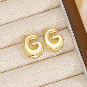 Gold sculptural stud earrings in the shape of the letter G.