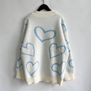 White acrylic knit sweater with pastel blue heart outline pattern and cream ribbed trim.