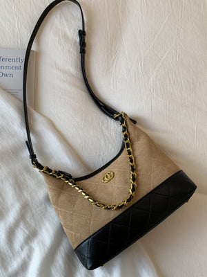 Half-moon crossbody bag in tan with black trim and gold chain detail.