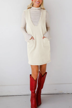 Cream sleeveless knit dress with V-neck and patch pockets, styled with a long sleeve top.