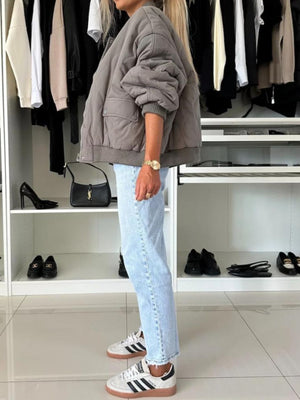 Quilted bomber jacket in taupe with rounded sleeves and front pockets, styled with light wash jeans.
