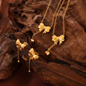 Gold bow drop chain earrings with heart charms and bead details.