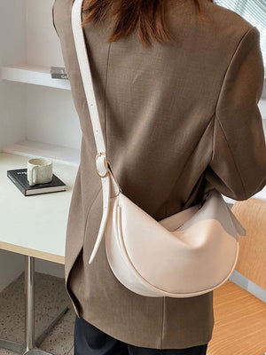 Crescent crossbody bag in beige white faux leather with adjustable strap.
