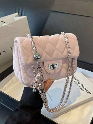Pink quilted crossbody clutch with silver chain strap and ball charm detail.
