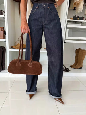 Dark blue denim wide-leg pants with cuffed hems and a brown suede shoulder bag.