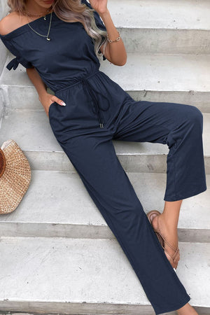 Off-the-shoulder navy jumpsuit with tie sleeves, drawstring waist, and pockets.
