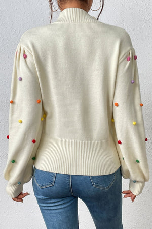 Cream blouson knit sweater with colorful pom-pom embellishments on sleeves.