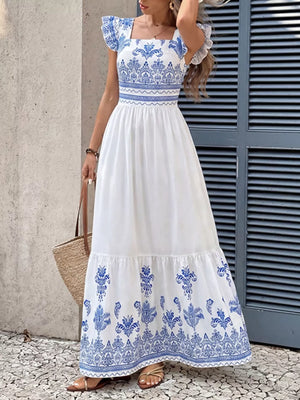 White maxi dress with royal blue print, square neck, flutter sleeves, and tiered hem.