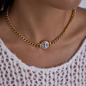 Gold curb chain necklace with vintage coin charm, styled with a white knit top.