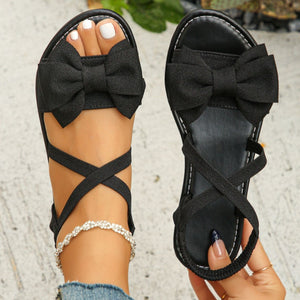 Black crisscross bow sandals with ankle straps and a jeweled anklet.
