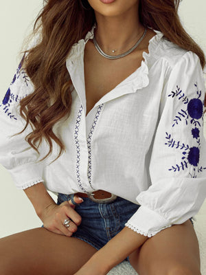 White linen blouse with blue embroidery, ruffled neckline, and scalloped trim.
