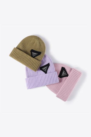 Ribbed acrylic beanies in khaki, purple, and pink, each with a black triangle patch.