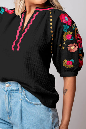 Black blouse with voluminous embroidered sleeves and pink neckline detail.