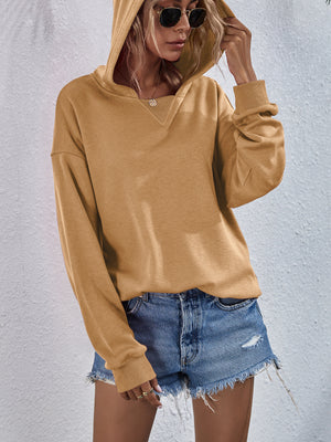 Tan boxy hooded sweatshirt with V-neck detail and split hem, styled with denim shorts.