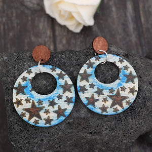 Multicolor celestial starburst wood hoop earrings with brown star pattern on blue sky background.