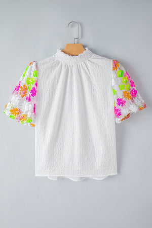 White textured blouse with puff sleeves featuring colorful sequin floral embroidery and a mock neck.