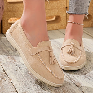 Beige faux-suede slip-on loafers with decorative tassels and a bow detail.