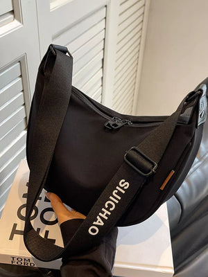 Black crescent crossbody bag with adjustable strap featuring white text detail