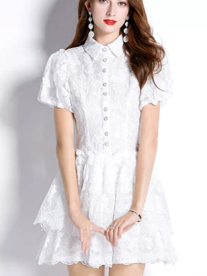 White lace mini dress with puff sleeves, buttoned front, and tiered skirt.